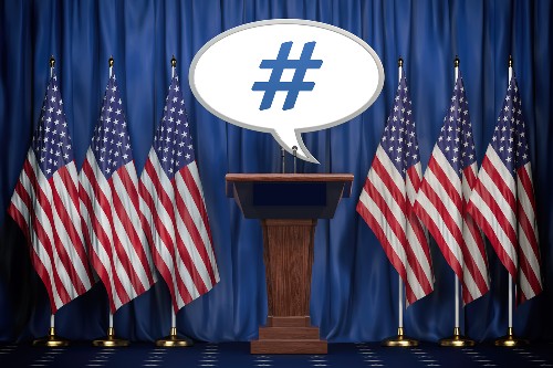US flag stands beside a podium with a hashtag in a speech bubble above it